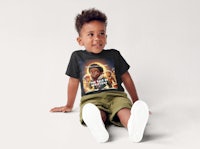a young boy sitting on the floor wearing a black t - shirt
